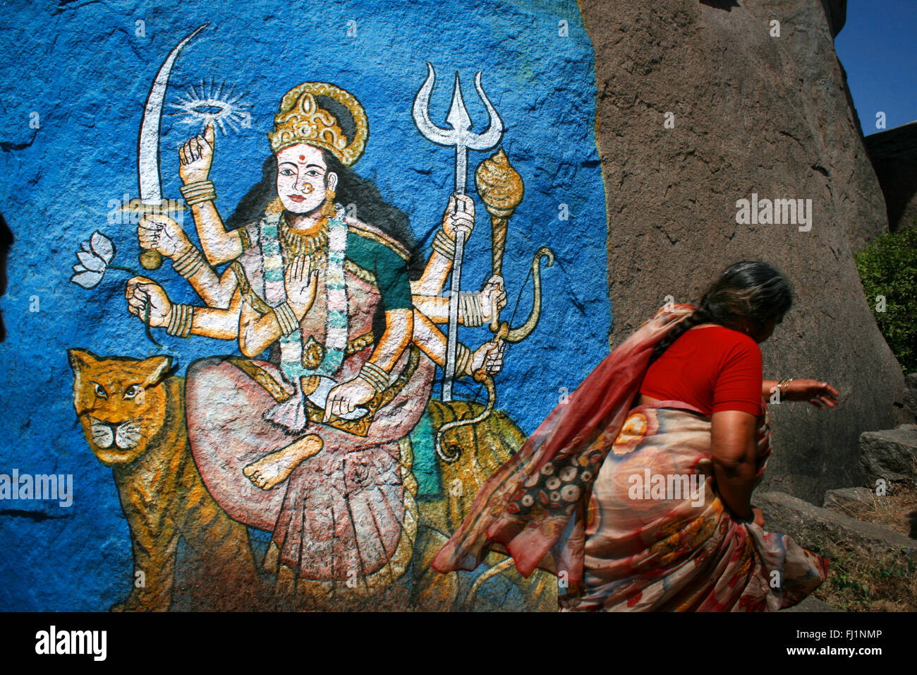 Woman with red saree walks in front of a painting of Hindu Goddess Durga in Hyderabad , India Stock Photo