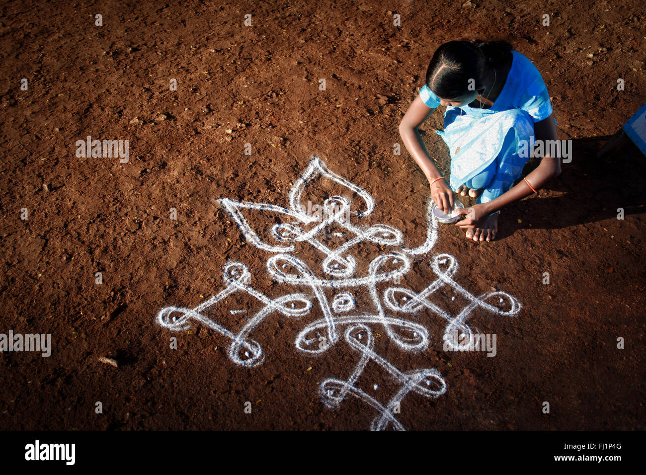 Woman is drawing rangoli in front of her house in the early morning light in Hampi, India Stock Photo