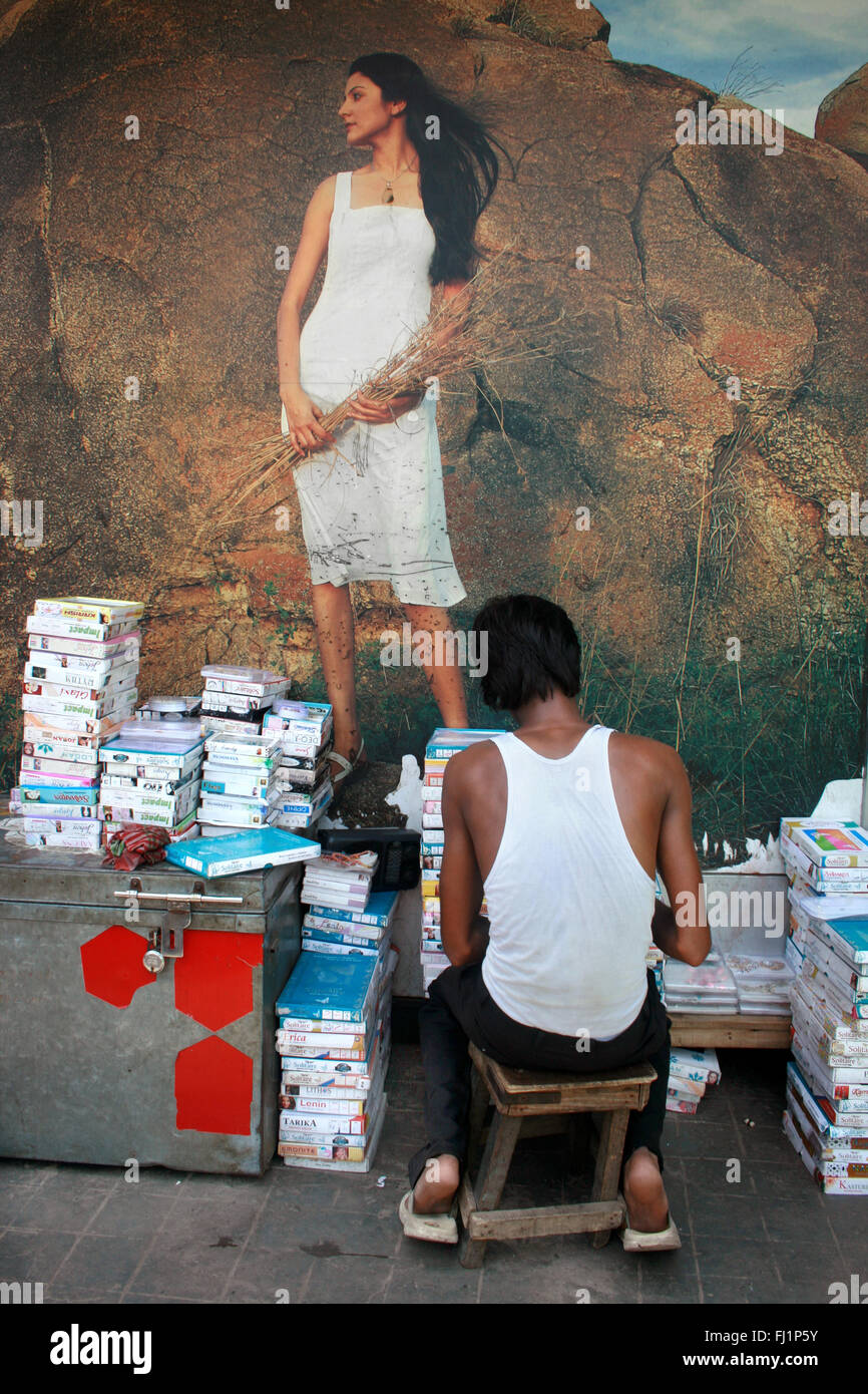 Lonely man selling books in front of a romantic poster of a beautiful indian woman Stock Photo
