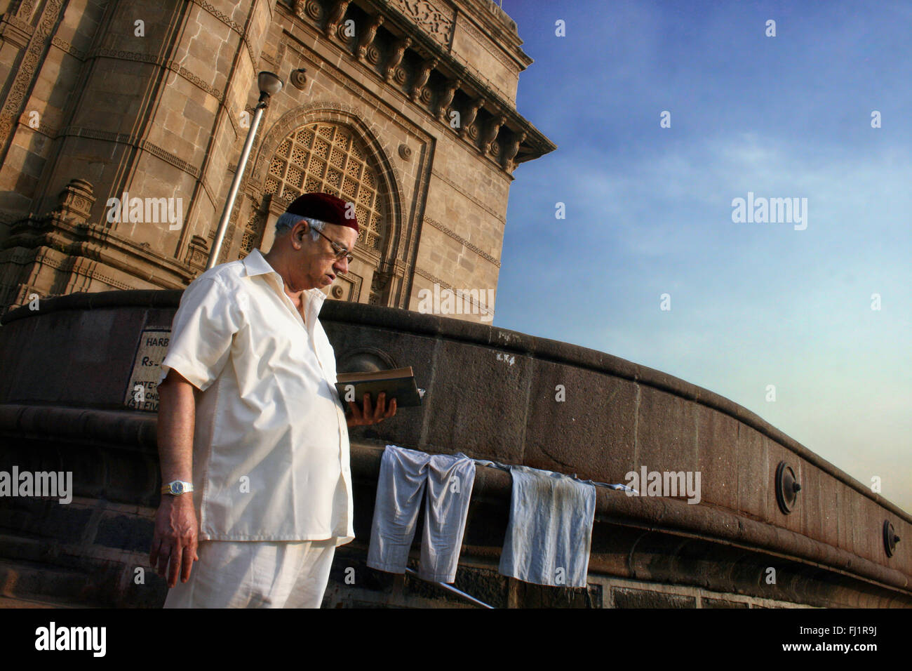 A man reads a book in the early morning light at the Gateway of India, Colaba , Mumbai, India Stock Photo
