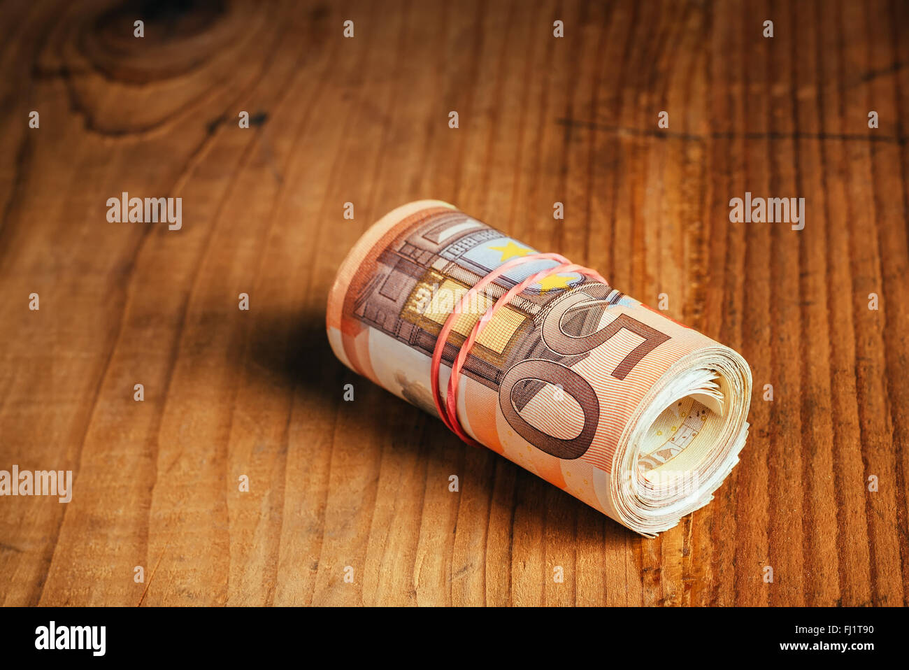 Saving money concept, rolled up cash money with rubber band on wooden desk, fifty euro banknotes personal home budget stack Stock Photo