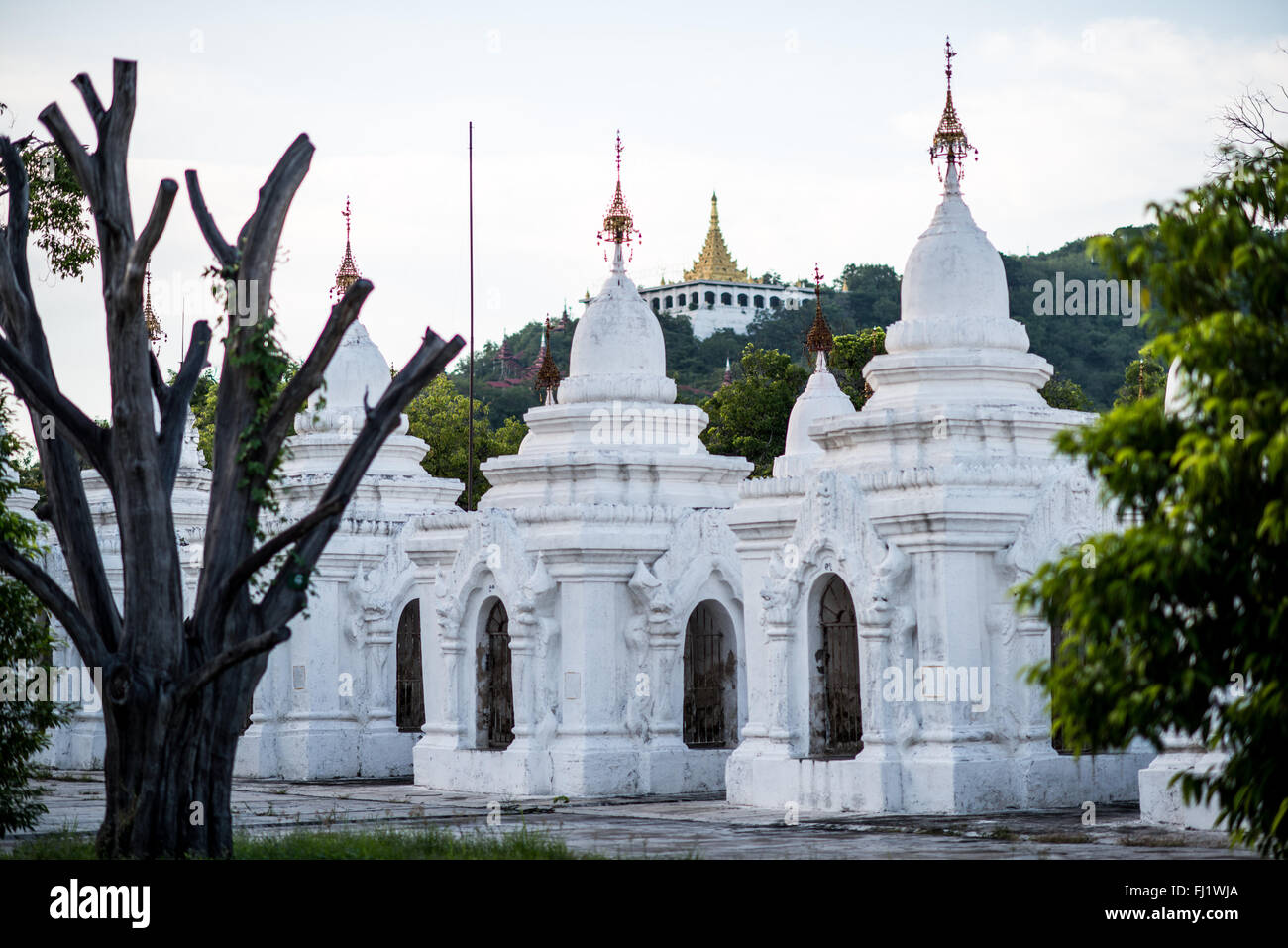 MANDALAY, Myanmar — Rows of pristine white kyauksa gu (stone-inscription caves) stretch across the grounds of Kuthodaw Pagoda. Built in 1857 by King Mindon, the complex contains 729 marble slabs that collectively form what is known as the World's Largest Book. Each small stupa houses a marble tablet inscribed on both sides with text from the Tipitaka, the complete Pali Canon of Theravada Buddhism. The orderly arrangement of these structures reflects traditional Buddhist architectural principles. Stock Photo