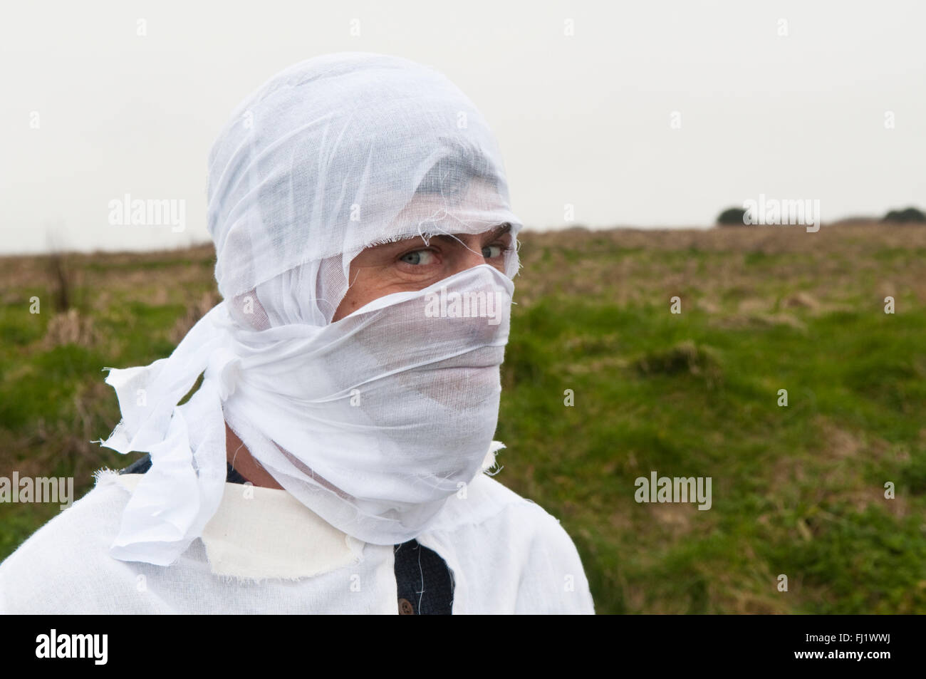 Man with his head in white bandages standing in a field Stock Photo