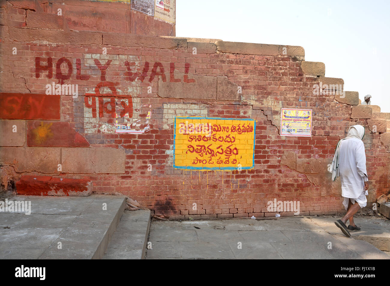 A man walks alone along a wall with 'Holy wall' writing in holy city Varanasi, India Stock Photo
