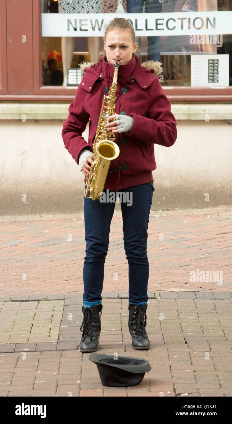 Young female saxophone playing busking on the street wearing fingerless gloves due to the cold February weather, Bournemouth Stock Photo