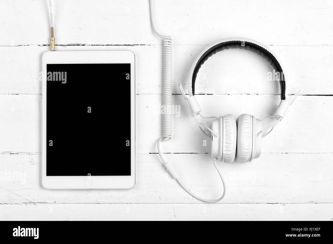 White tablet with headphones on white wooden background Stock Photo