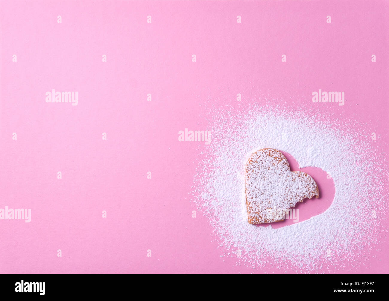 Heart shaped cookie with sugar icing on a pink paper background taken a bite from it Stock Photo