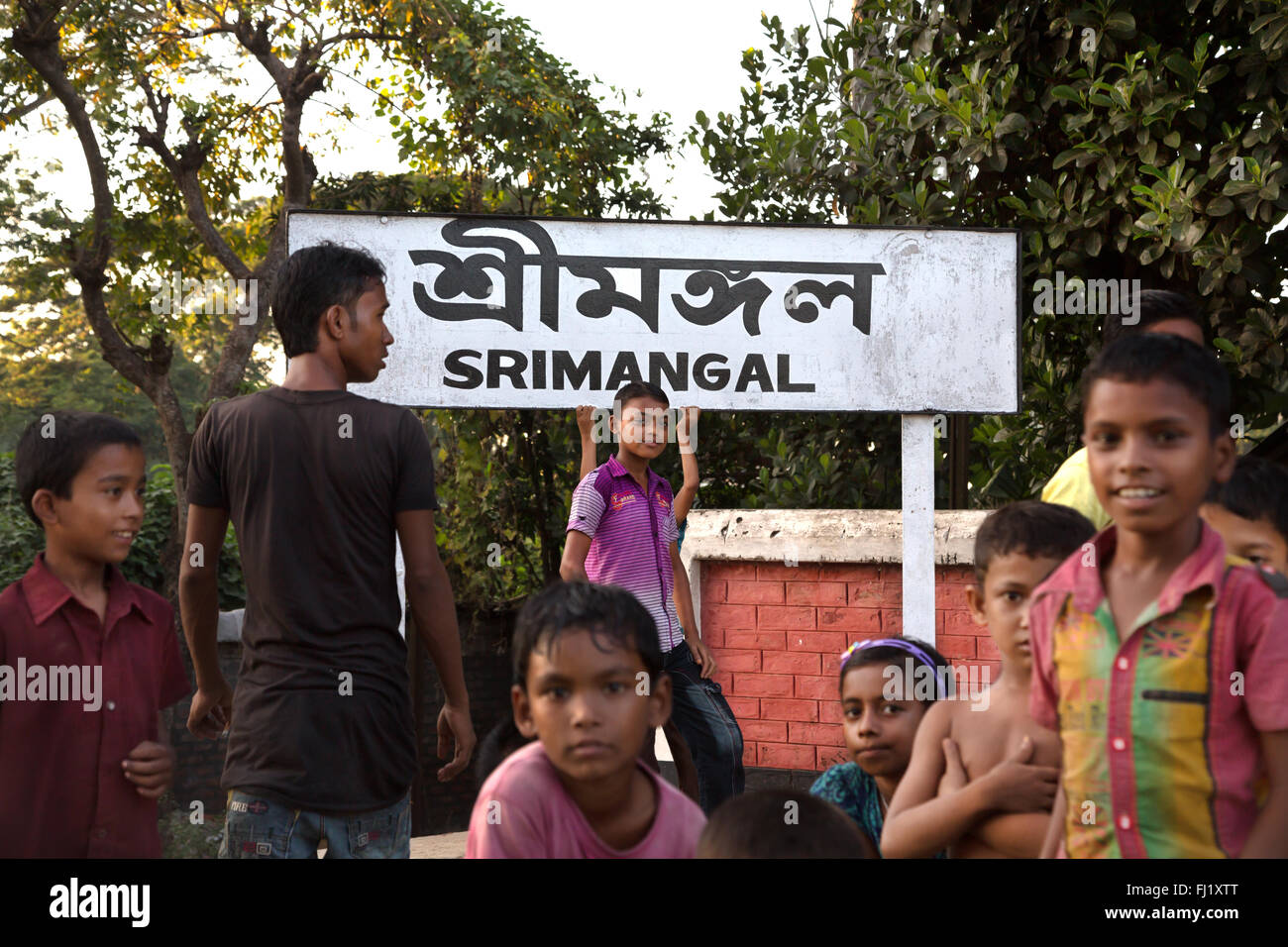 A group of kids stand at Sreemangal railway station in front of board 'Srimangal' in bengali language, Bangladesh Stock Photo