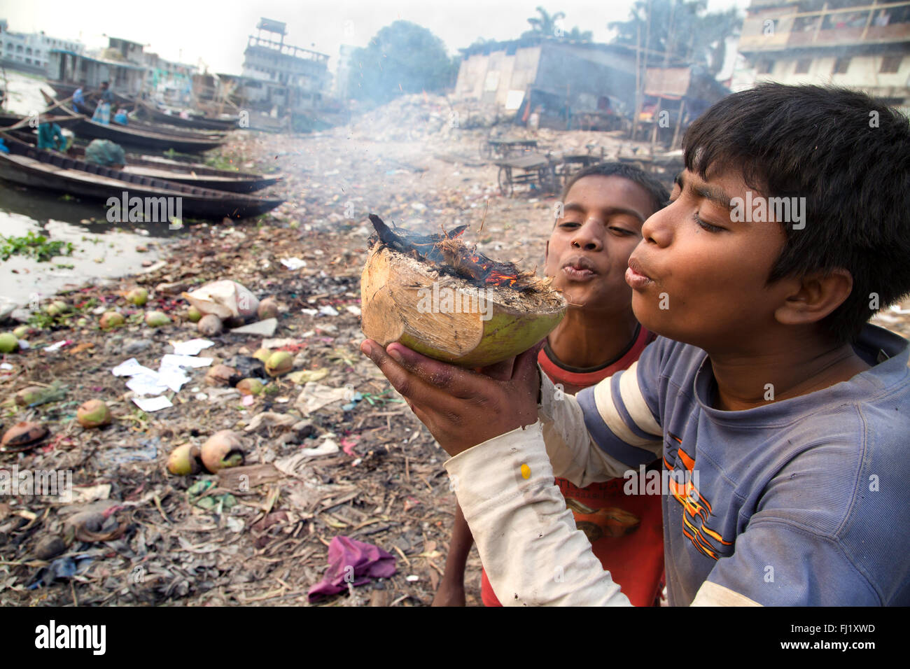 Two kids blow on a coconut on fire at Sadarghat , Bangladesh Stock Photo