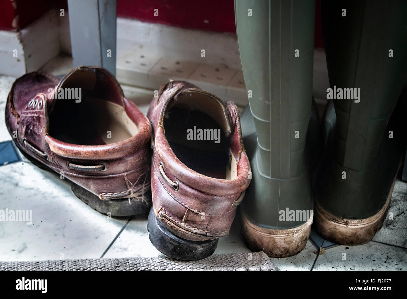 Pair of leather shoes and a pair of muddy boots together on the floor in the corner of a room Stock Photo