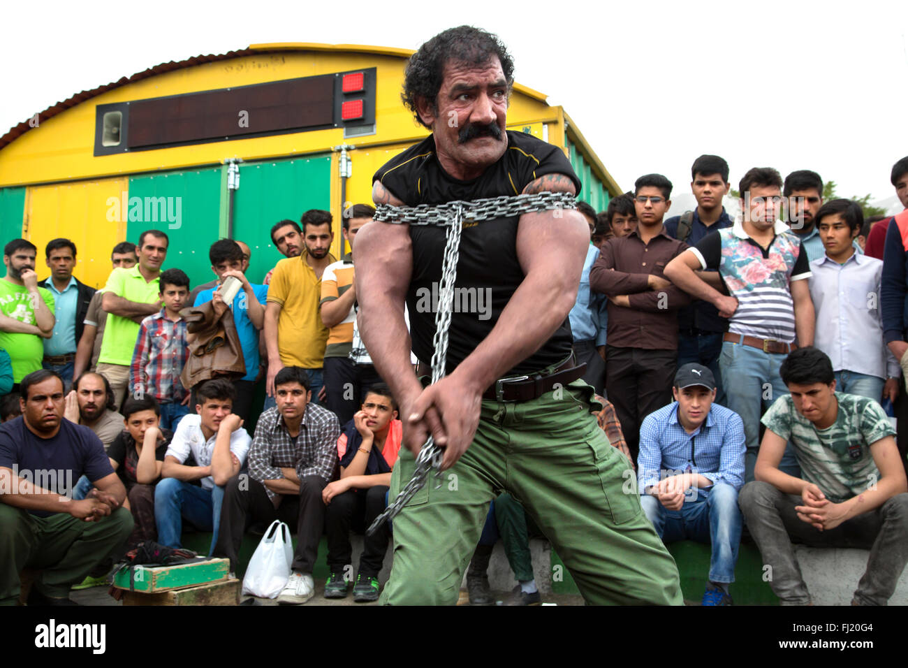 A man theatrically struggles to break free of chains in front of the Imamzadeh Saleh mausoleum, Tehran , Iran Stock Photo