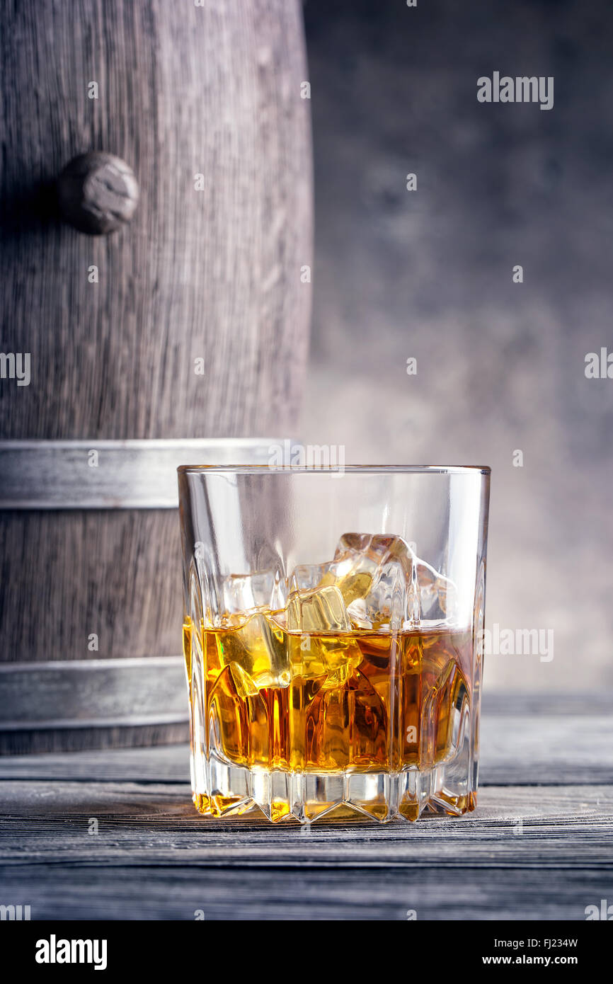 Round glass of whiskey with ice cubes against the background of wooden barrels Stock Photo