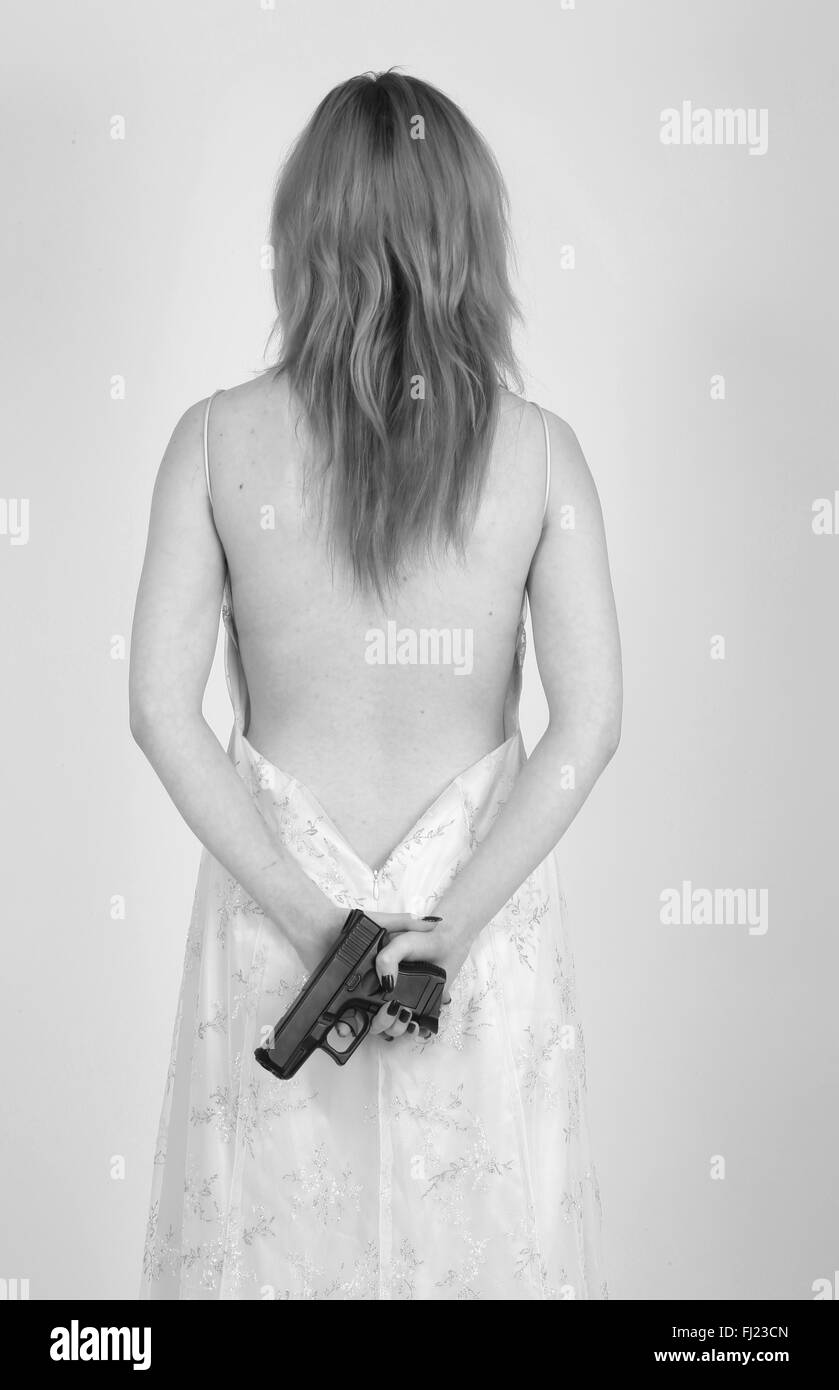 Young redheaded woman (19 years old) in a cute backless evening dress holding a pistol. Stock Photo