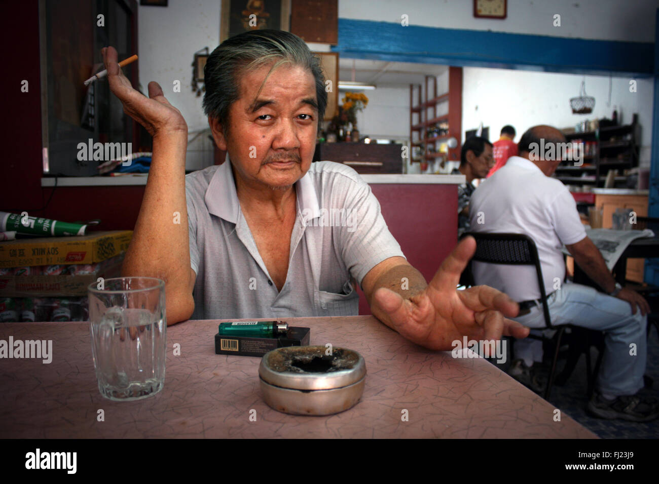 Portrait of a old man in Kuala Lumpur sitting in a restaurant and smoking a cigarette Stock Photo