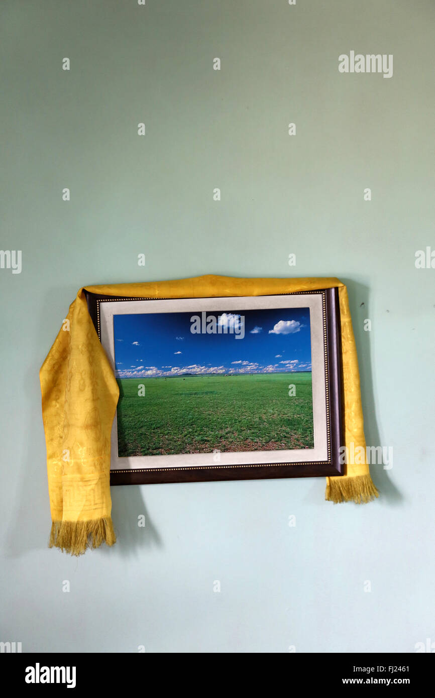 Frame hanging  on the wall in typical Mongolian house, with countryside picture in it and yellow khata on it for protection Stock Photo