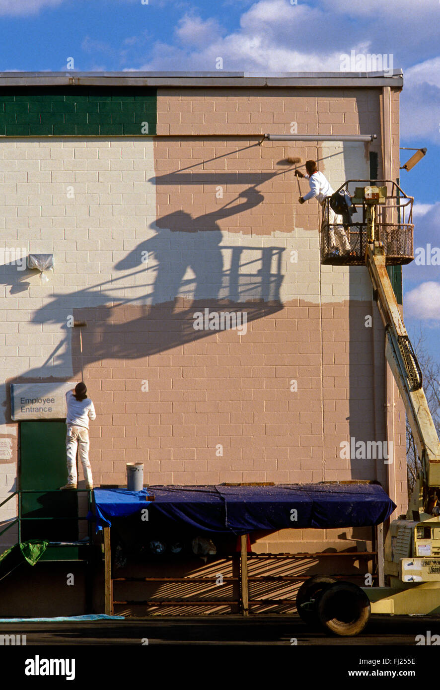 Professional painters on lift apply latex paint to warehouse exterior Stock Photo
