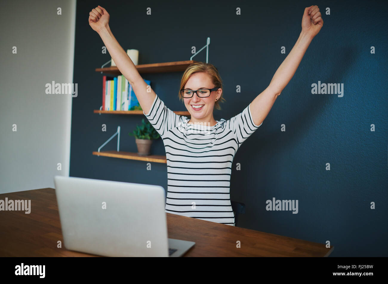 Female entrepreneur at home office with arms raised in success sitting with a laptop Stock Photo