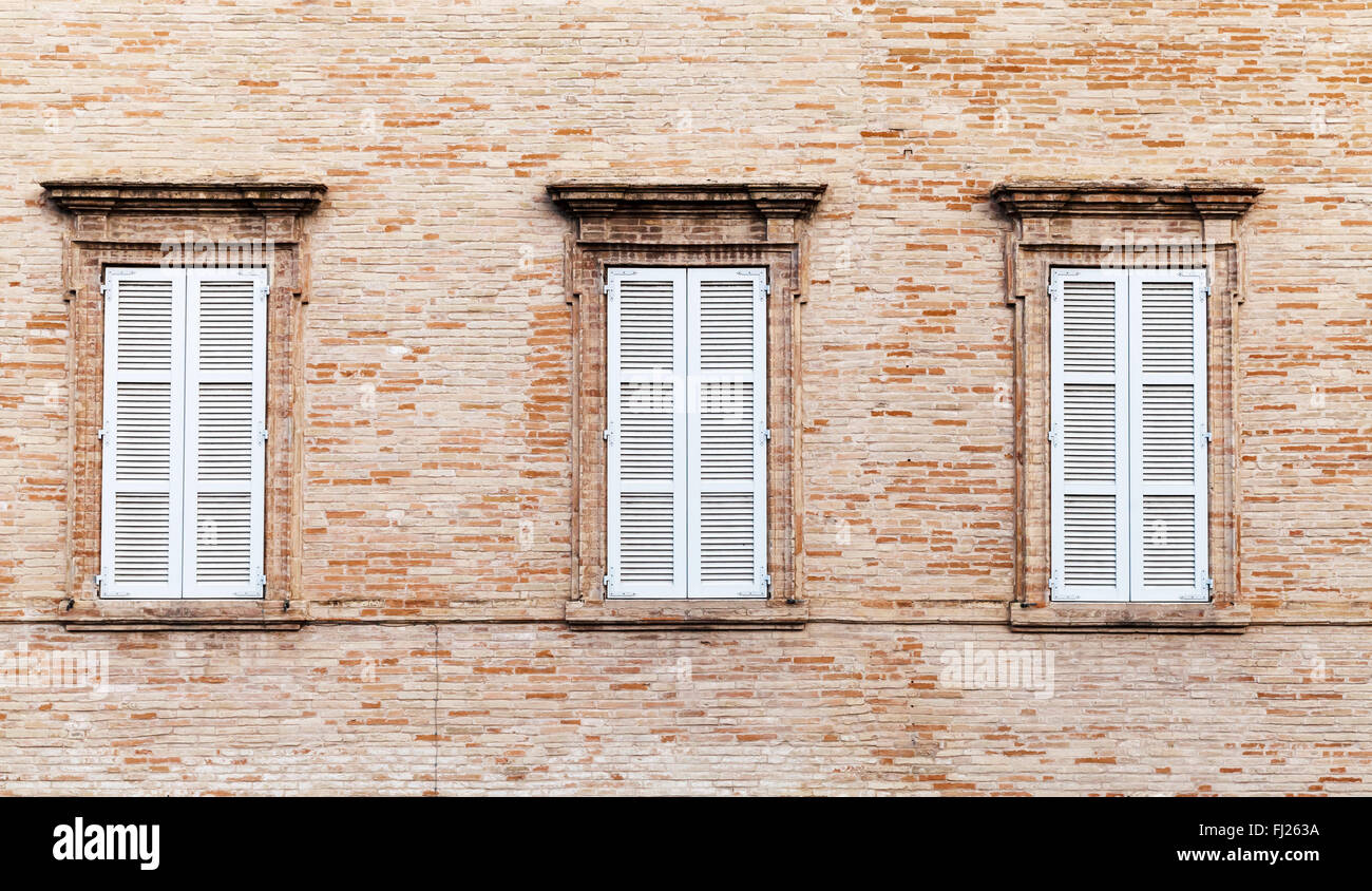 Three windows with white closed wooden shutters in old brick wall, background photo texture Stock Photo