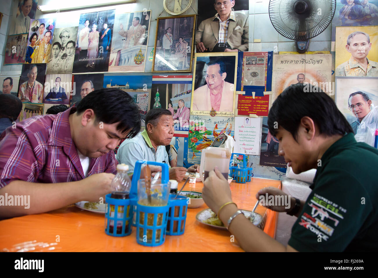People eating in a traditionnal streetfood place in Bangkok with pictures of King Bhumi on the wall, Thailand Stock Photo