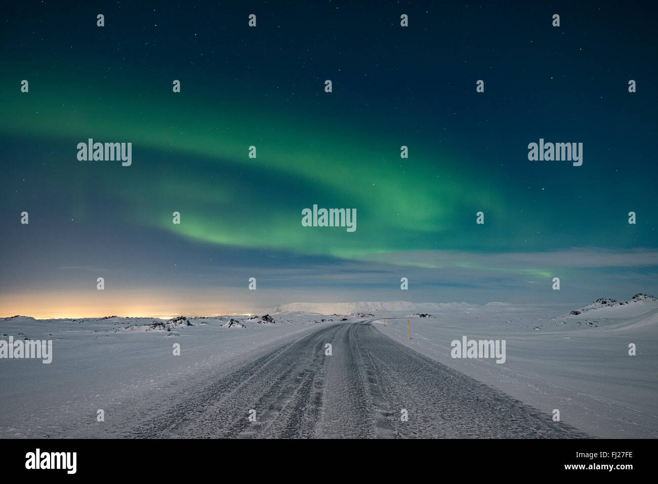The northern lights dancing in the sky above a frozen mountain road