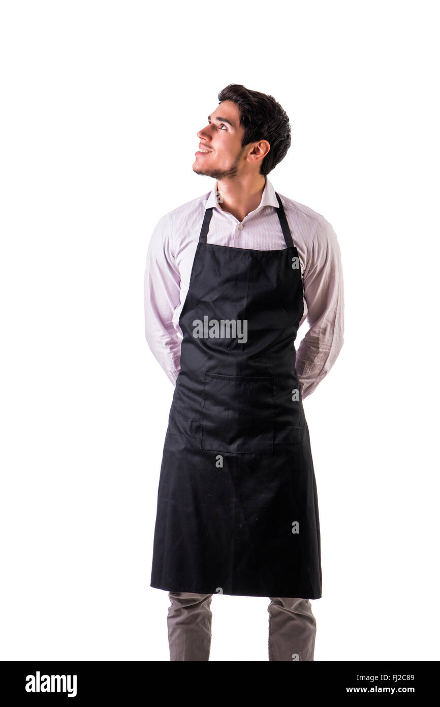 Young chef or waiter posing, wearing black apron and shirt isolated on white background, looking up to a side Stock Photo