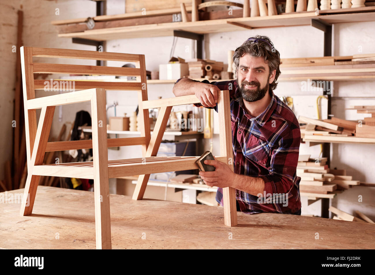 Artisan furniture designer sanding a chair in his Stock Photo