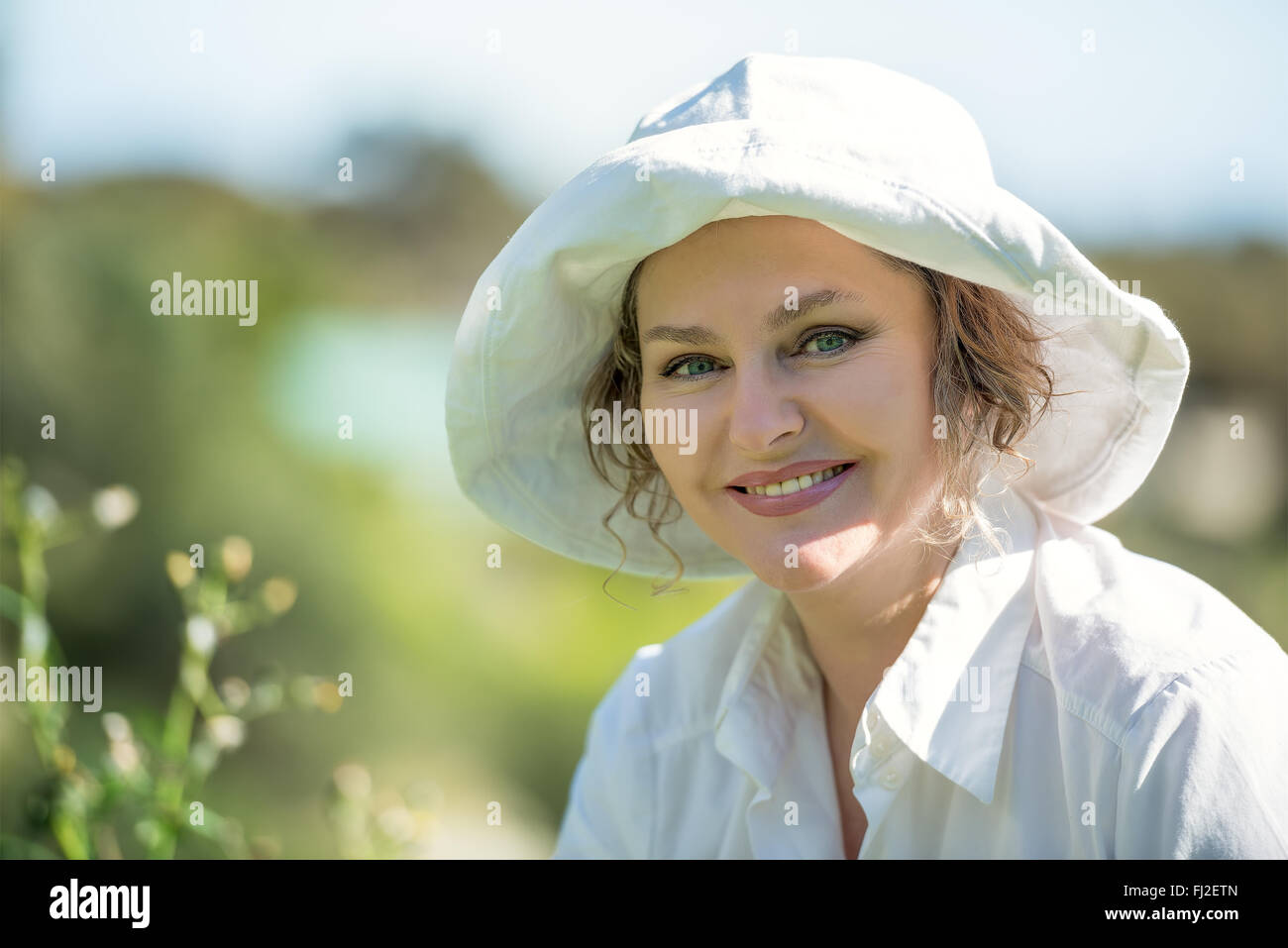 Happy woman in white hat and shirt is smiling outdoors Stock Photo