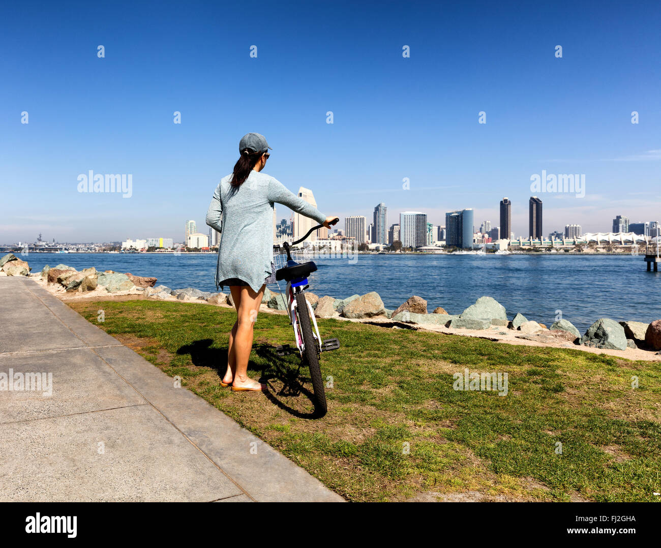 Back view of a woman, holding bicycle, will looking at the bay of San Diego in Southern California. Stock Photo