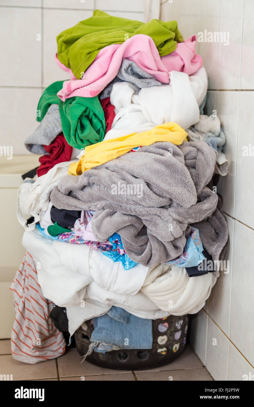 Laundr basket overflowing with dirty clothes and blankets Stock Photo