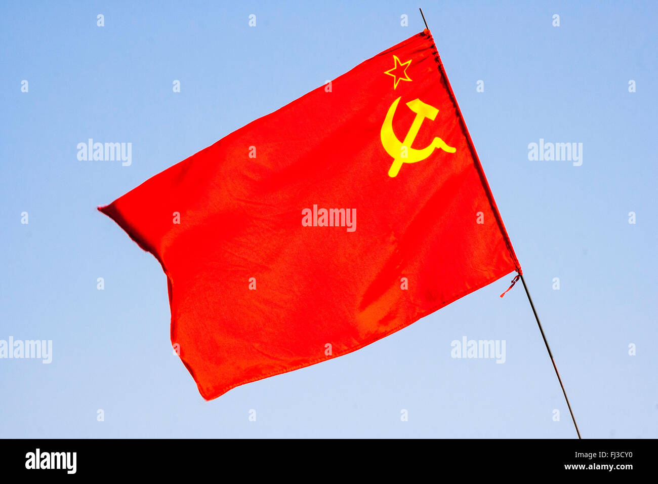 Communist flag of Russia, USSR, red flag, hammer and sickle in yellow, against plain blue sky background Stock Photo
