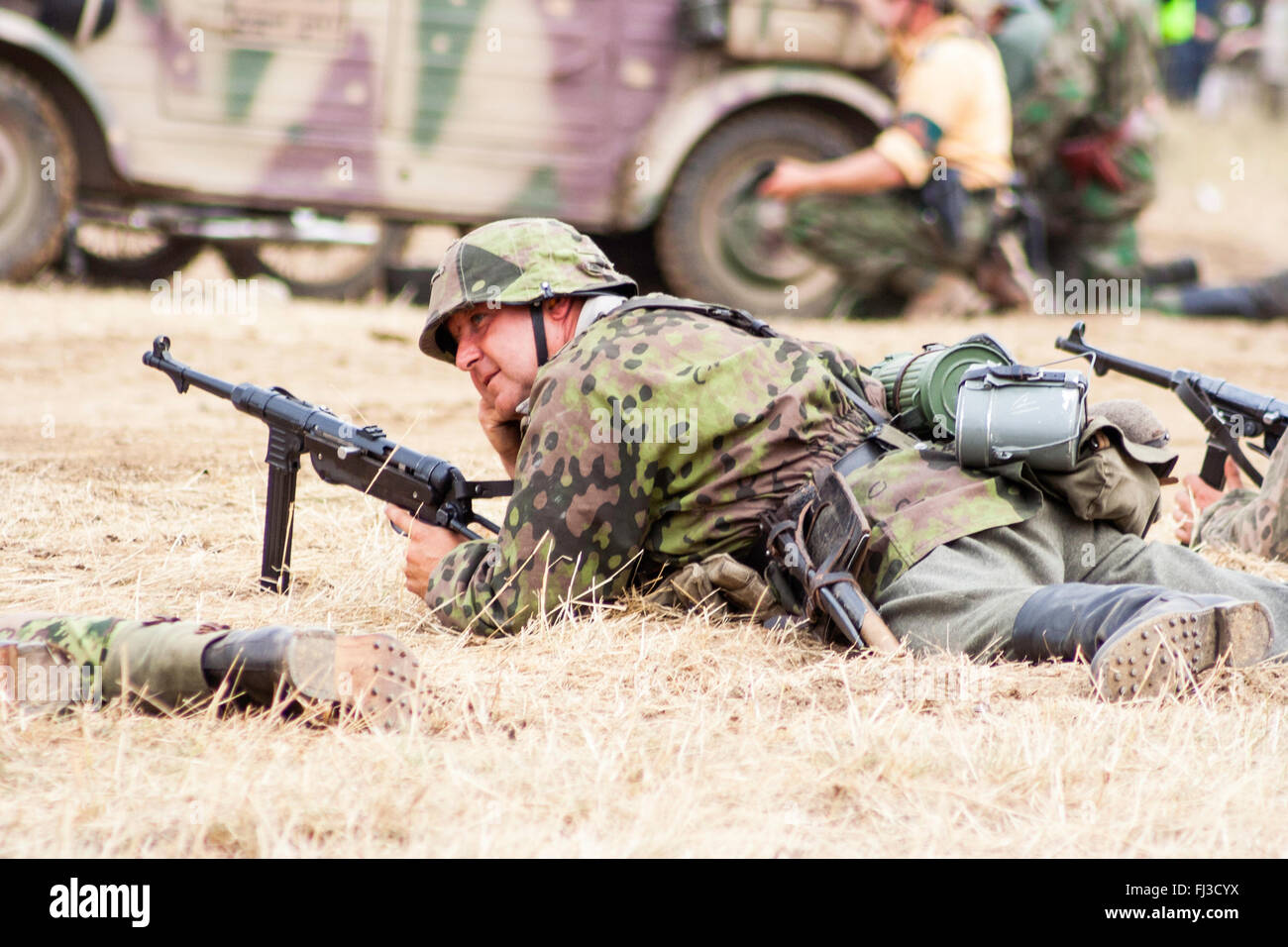 Swcond world war re-enactment. German Waffen SS soldier in dot camouflage uniform, laying in grass, holding MP 40 sub machine-gun during mock battle. Stock Photo
