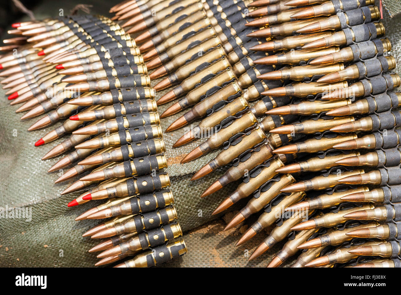 Various types of Machine gun rounds, some red-tipped, tracer bullets, in belts laid on top of sandbag. Close up. Stock Photo