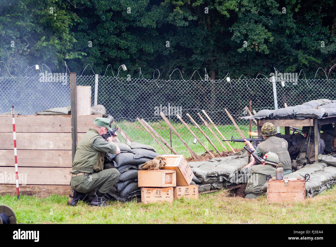 War and peace show, England. Vietnam war re-enactment. American fire base under attack by unseen enemy in woods, soldiers behind wire returning fire. Stock Photo