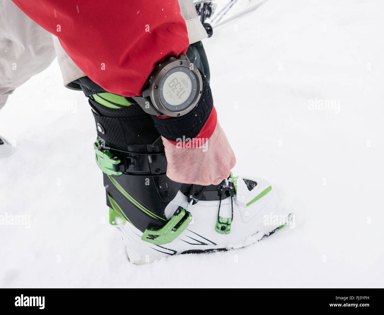 Skier adjusting alpine touring ski boots and wearing a Suunto Traverse GPS Watch device for backcountry navigation. Alps Stock Photo