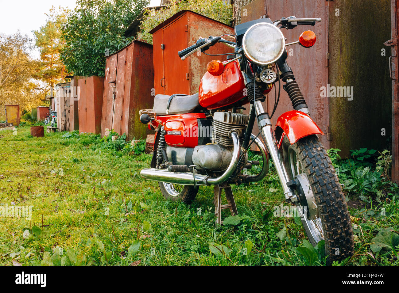 Old Red Russian Soviet Motorcycle Voshod Parked On Green Grass. This motorcycles produced at Degtyarev plant in Russian town Stock Photo