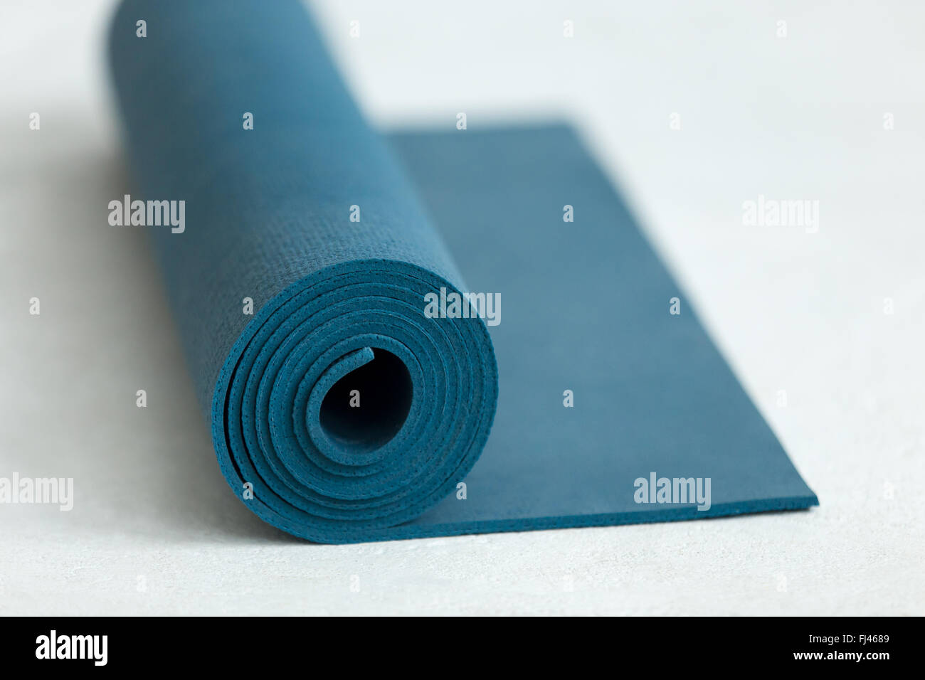 Rolled up blue yoga, pilates or exercise mat on the floor, close up Stock Photo