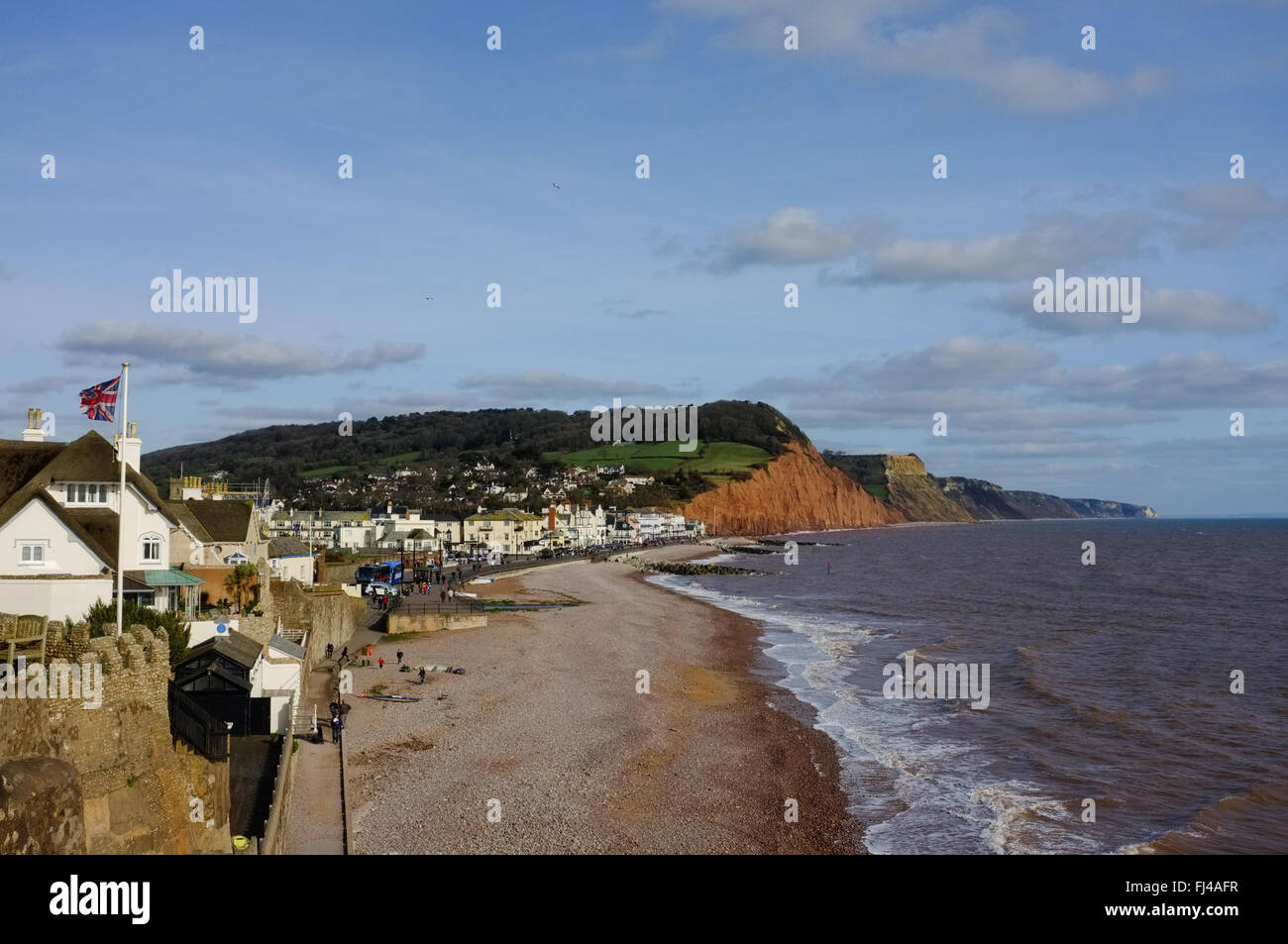 View of Sidmouth coastline and town with people walking on the beach with cliffs in the background. Stock Photo