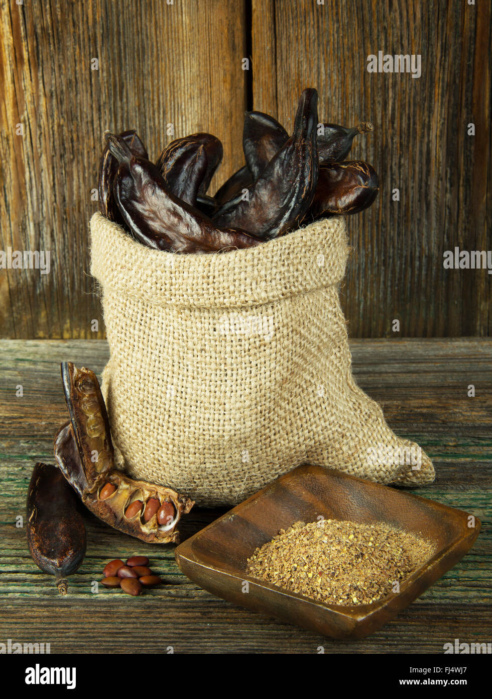 Carob pods in linen bag on wooden background Stock Photo