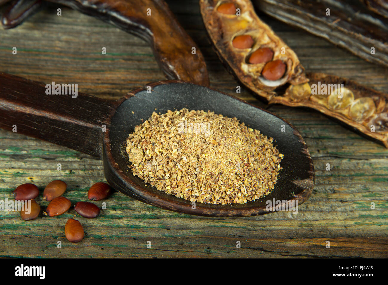 Grounded carob grains on wooden spoon Stock Photo