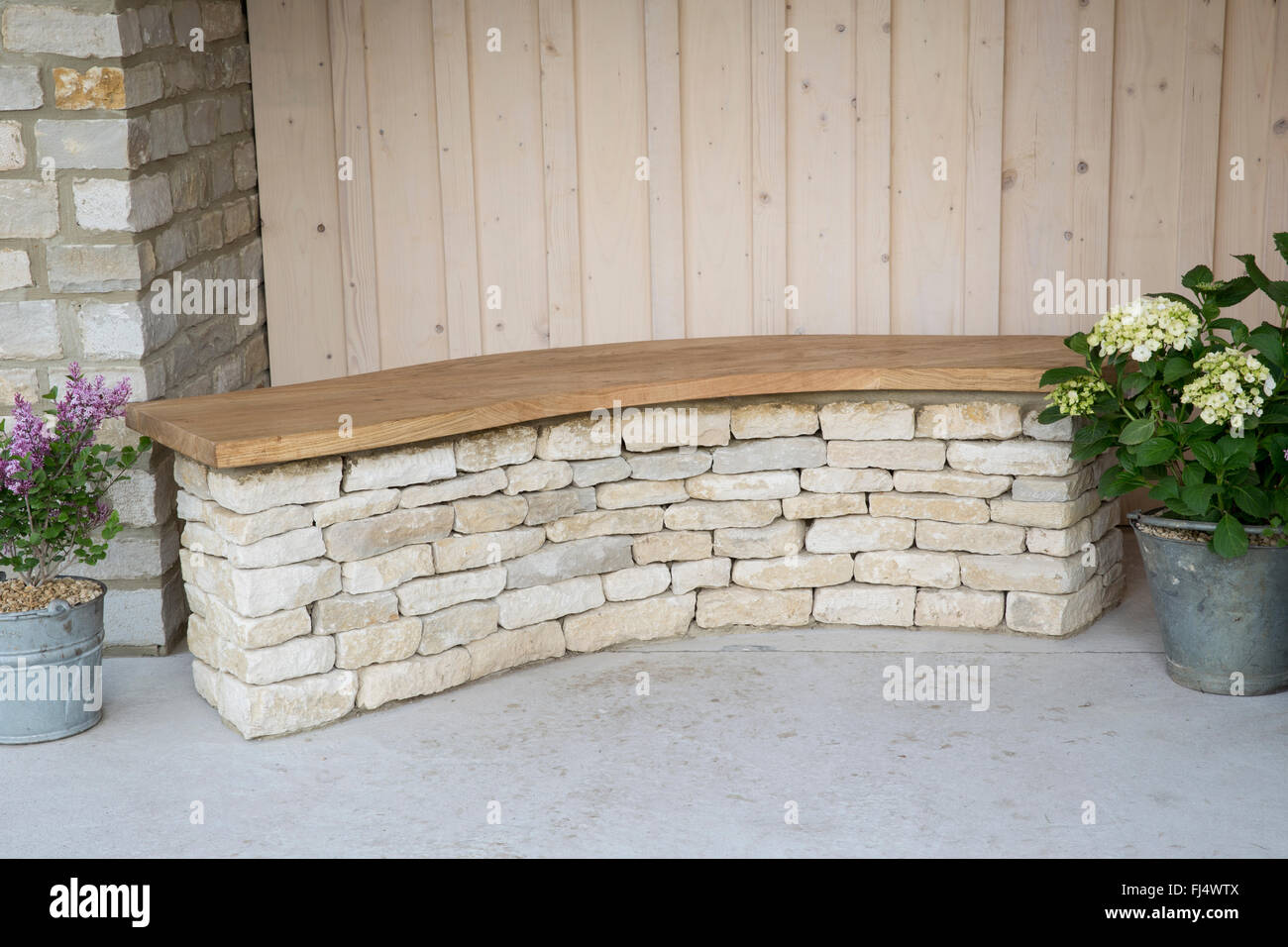 Cotswold stone bench with wooden seat, Hydrangea in galvanised metal bucket - The Cotswold Way garden - Designer: Amy Perkins Stock Photo