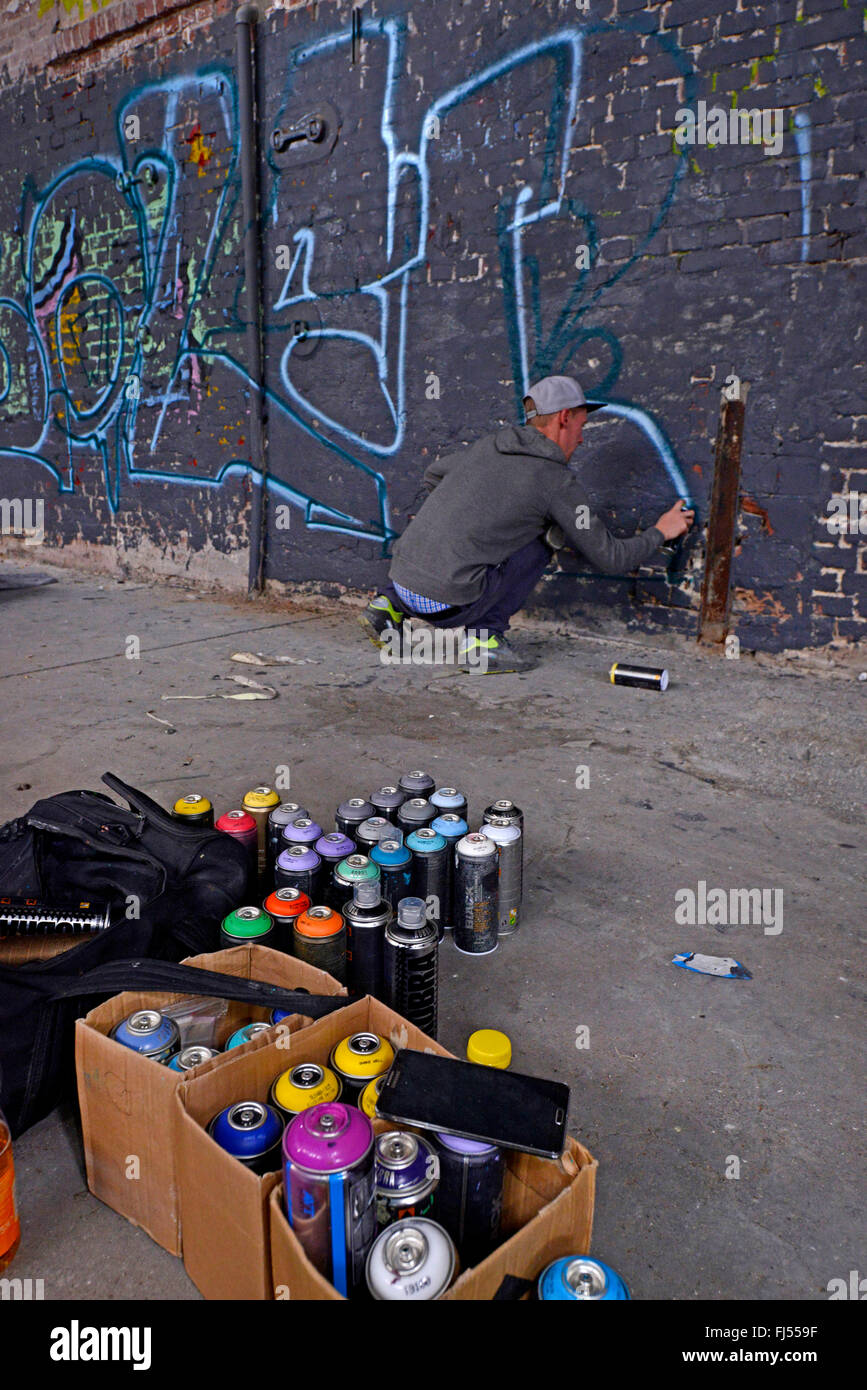man spraying graffiti at a wall in an abandonend industrial ground, Germany, North Rhine-Westphalia, Duesseldorf Stock Photo