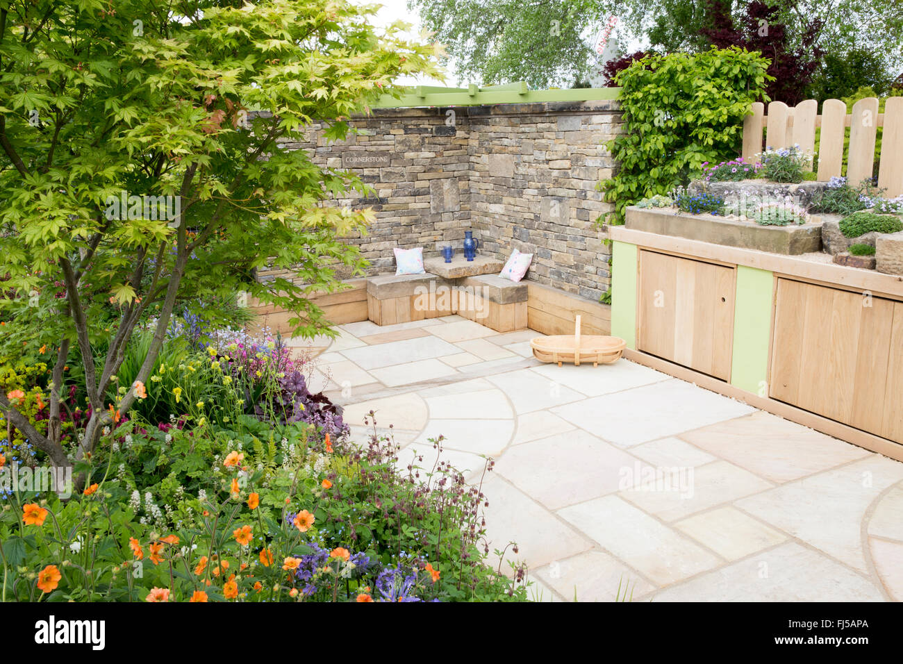 A small English garden with flower beds and a stone slabs patio - storage bench - stone bench and alpine plants in stone troughs containers Spring UK Stock Photo