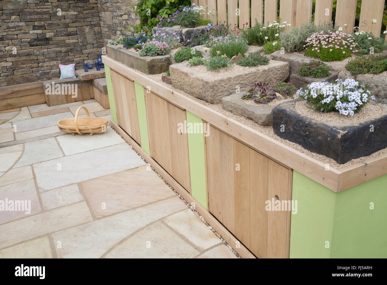 Small urban garden stone slabs patio storage cupboards a display of alpine plants in stone troughs containers container - seating area stone bench UK Stock Photo