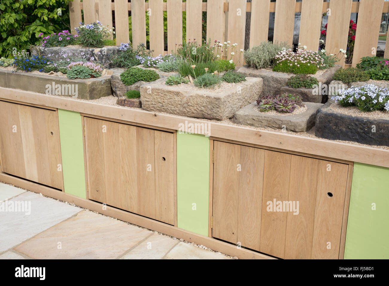 Patio with a rock garden with alpine plants plant in stone trough troughs and bench with storage cupboards - spring UK Malvern flower show festival Stock Photo
