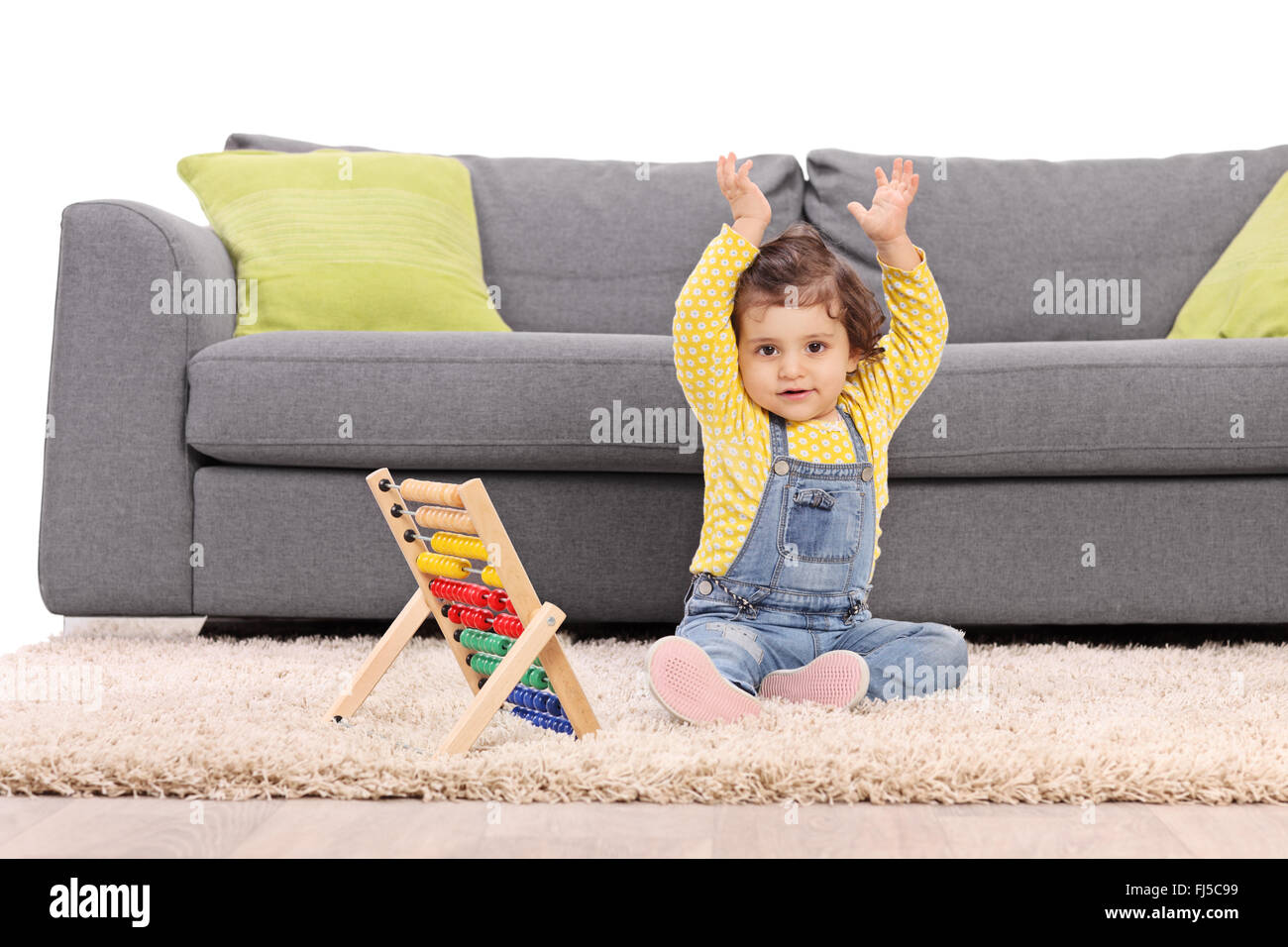 Baby girl sitting on floor in front of a gray sofa and gesturing with her hands with an abacus next to her Stock Photo