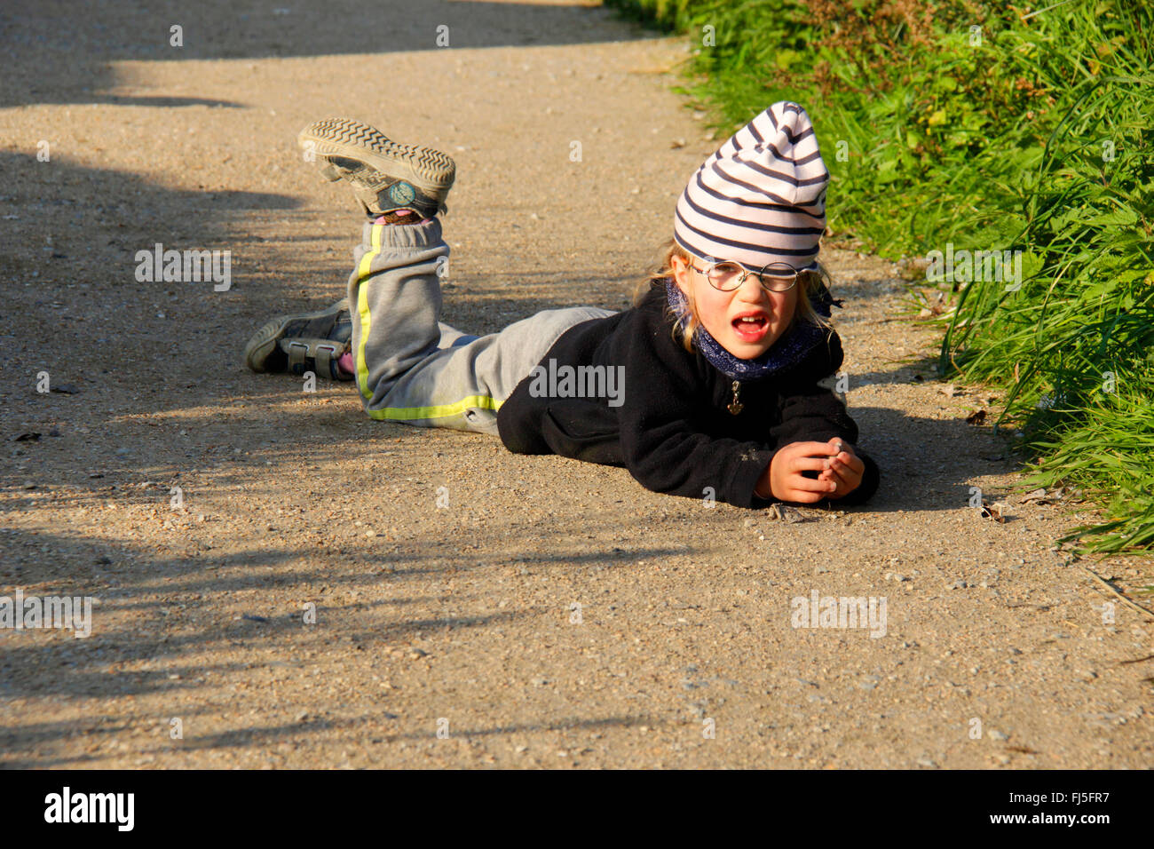 defiant little girl lying on a path Stock Photo