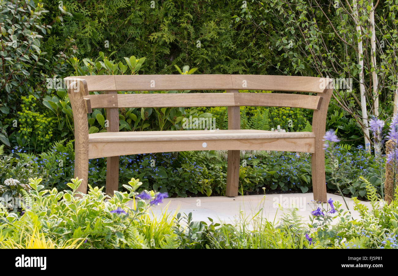 Small garden with seating area an oak wooden wood garden bench made by Gaze Burvill on a stone paved patio at RHS Malvern Spring Show UK Stock Photo