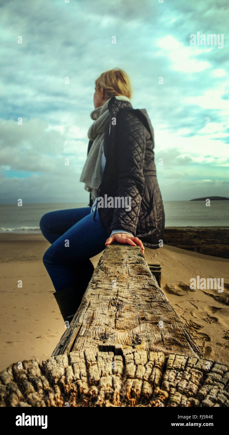 young woman sitting on wood on beach Stock Photo