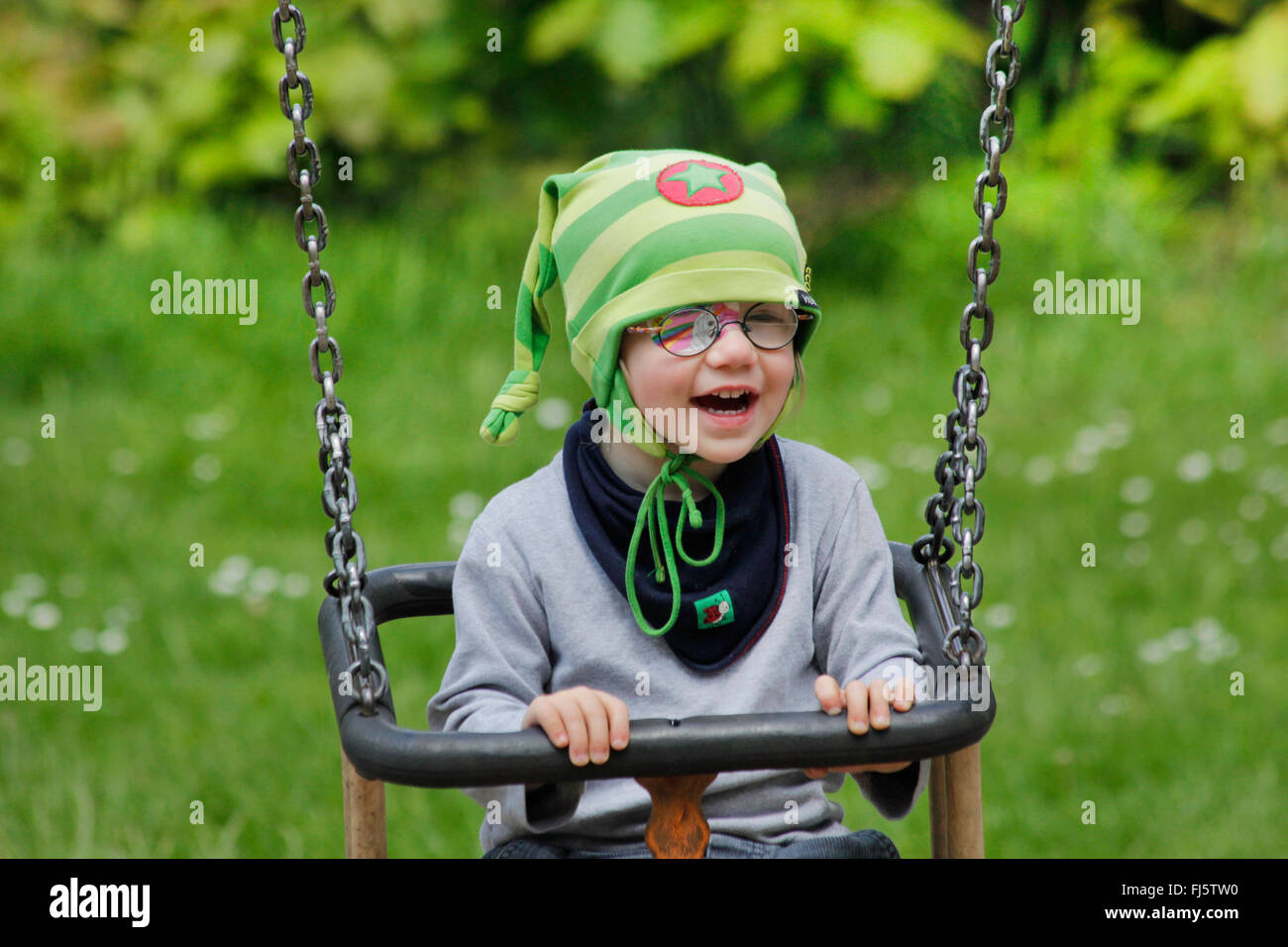 little girl with eye patch sitting amused in a swing, Germany Stock Photo