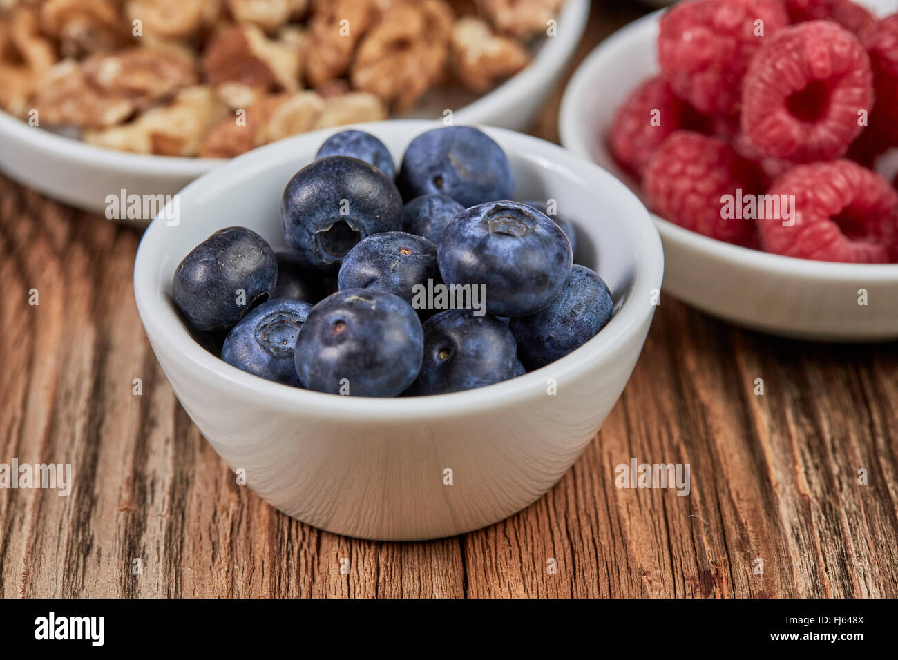 Bilberries and other super food in white china dishes on a brown wooden table Stock Photo